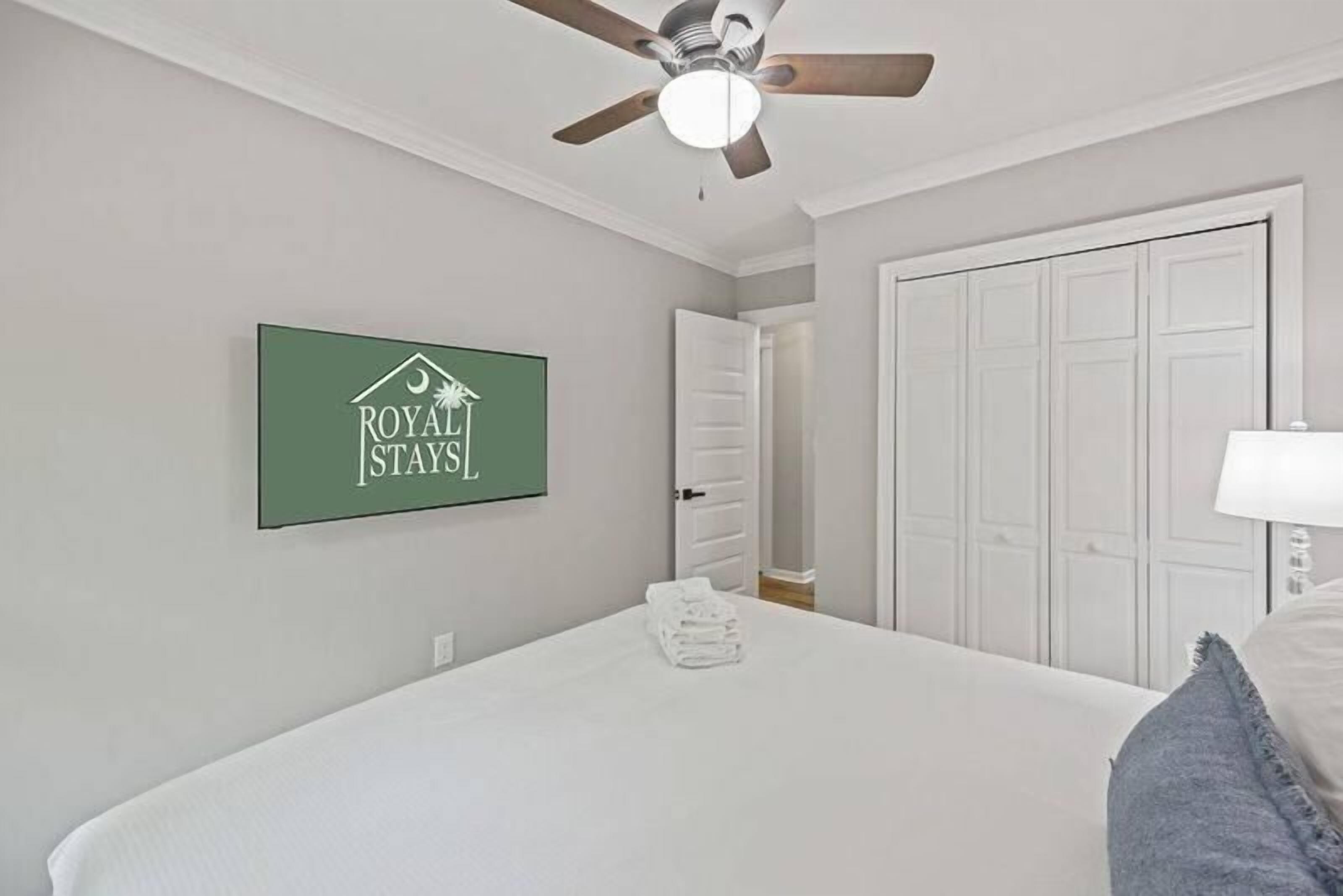 Habitación de hotel con cama, ventilador de techo, un cartel verde en la pared y una puerta que da a otra habitación.