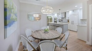 Un coin repas avec une table ronde en bois entourée de chaises en osier, un lustre et un grand tableau abstrait accroché au mur.