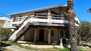 Un edificio di due piani con una scala in legno che conduce a un balcone, una palma sullo sfondo e un cielo azzurro limpido.