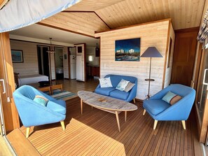 A room with a wooden floor, a blue sofa, a coffee table, and a lamp. - Chalet spacieux,grande terrasse exposée Est/sud, beaux espaces pour les familles (Gruissan)