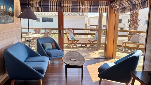 Un interno moderno con soffitto in legno, poltrone blu, un tavolino e vista sull'esterno.