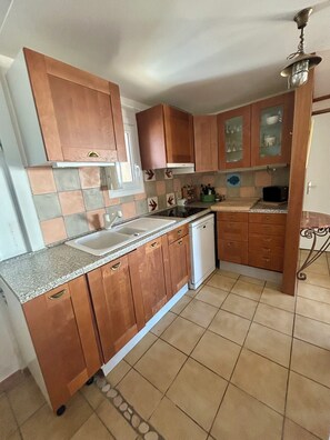 A kitchen with wooden cabinets, a built-in dishwasher, and a tiled backsplash. - Chalet spacieux,grande terrasse exposée Est/sud, beaux espaces pour les familles (Gruissan)
