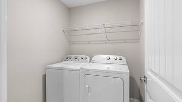 A laundry room with two front-loading washing machines and a metal drying rack.