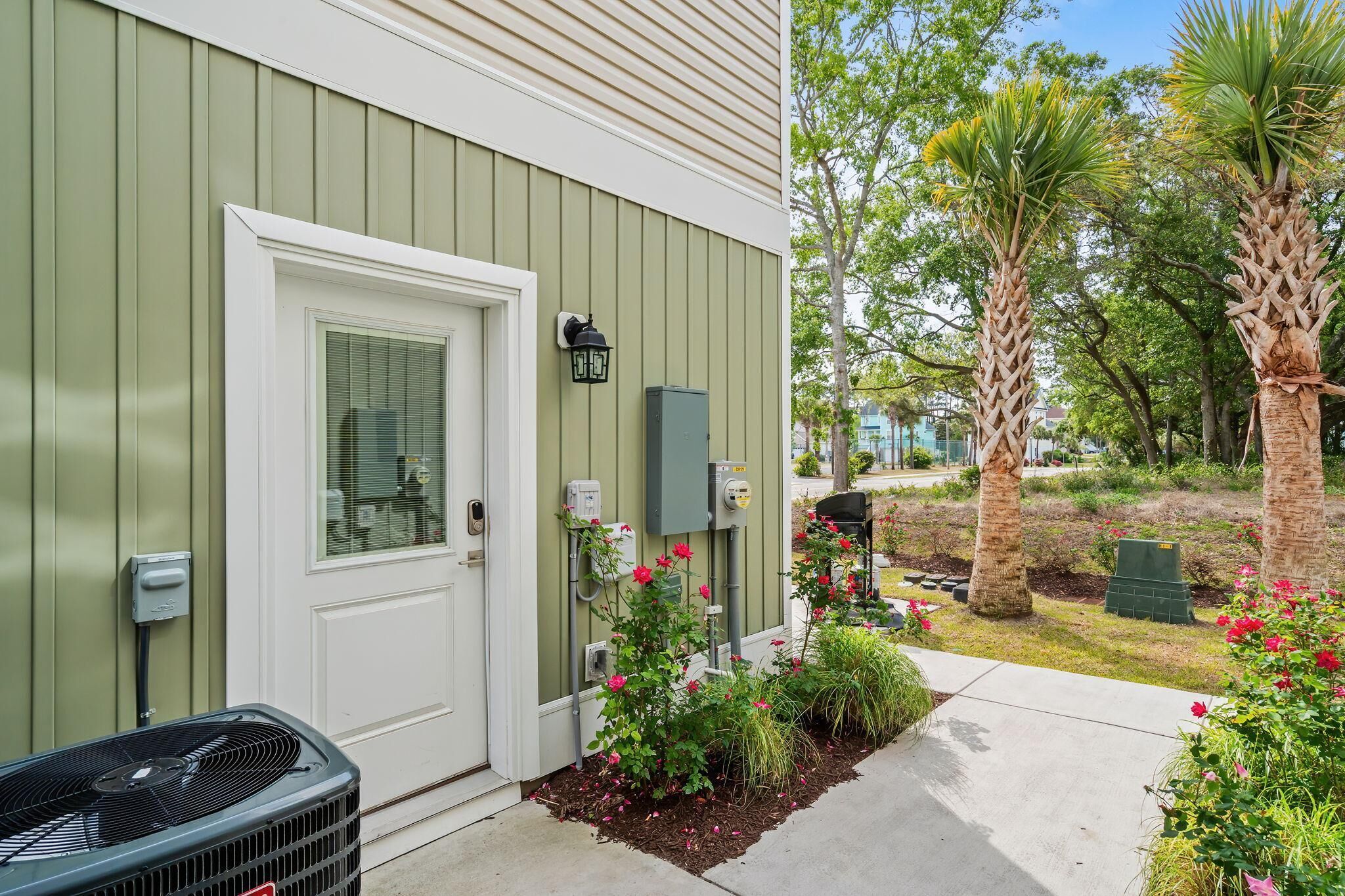A house with a green exterior, a white door, and a small garden with plants and flowers.
