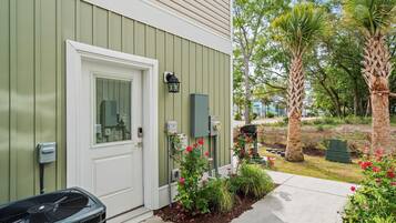 A house with a green exterior, a white door, and a small garden with plants and flowers.
