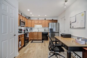 A modern kitchen with wooden cabinets, stainless steel appliances, a dining area with a table and chairs, and a whiteboard on the wall. - Adorable 2 Bedroom One Story Townhouse with Garage (High Point)