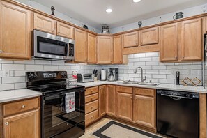 A modern kitchen with wooden cabinets, stainless steel appliances, a microwave, oven, toaster, sink, and dishwasher. - Adorable 2 Bedroom One Story Townhouse with Garage (High Point)