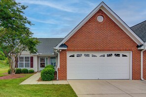 A two-story house with a brick facade, a white garage door, and a small front porch. - Adorable 2 Bedroom One Story Townhouse with Garage (High Point)