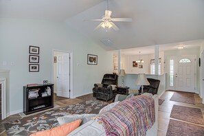 A spacious living room with a ceiling fan, a fireplace, a bookshelf, and a large window. - Adorable 2 Bedroom One Story Townhouse with Garage (High Point)