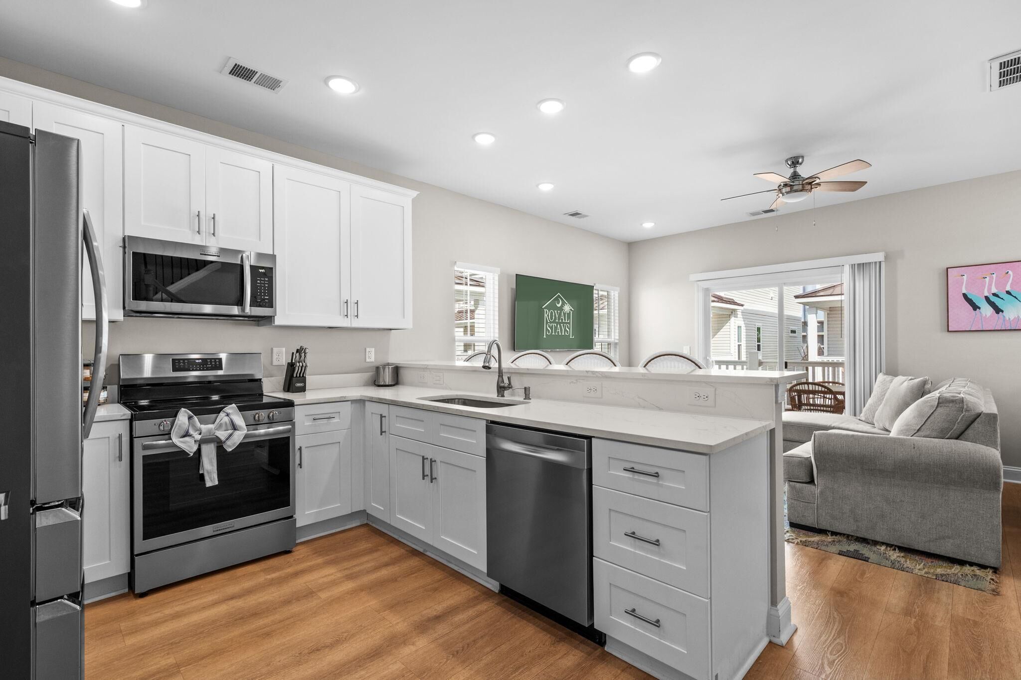 A modern kitchen with white cabinets, stainless steel appliances, and a wooden floor.