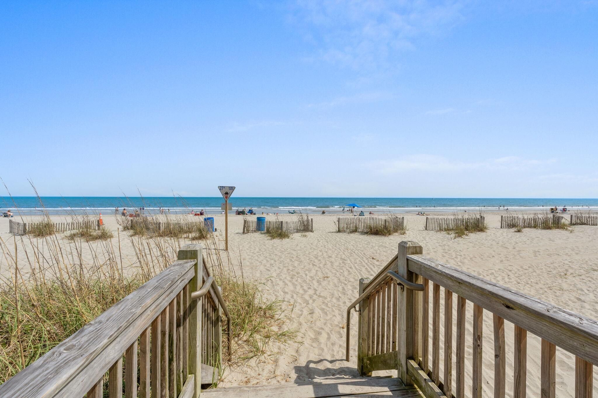 A wooden boardwalk leading to a sandy beach with a clear sky.