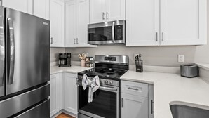A modern kitchen with white cabinets, stainless steel appliances, and a black stovetop. - The Pink Panther-ocean Side-pet Friendly (Myrtle Beach)