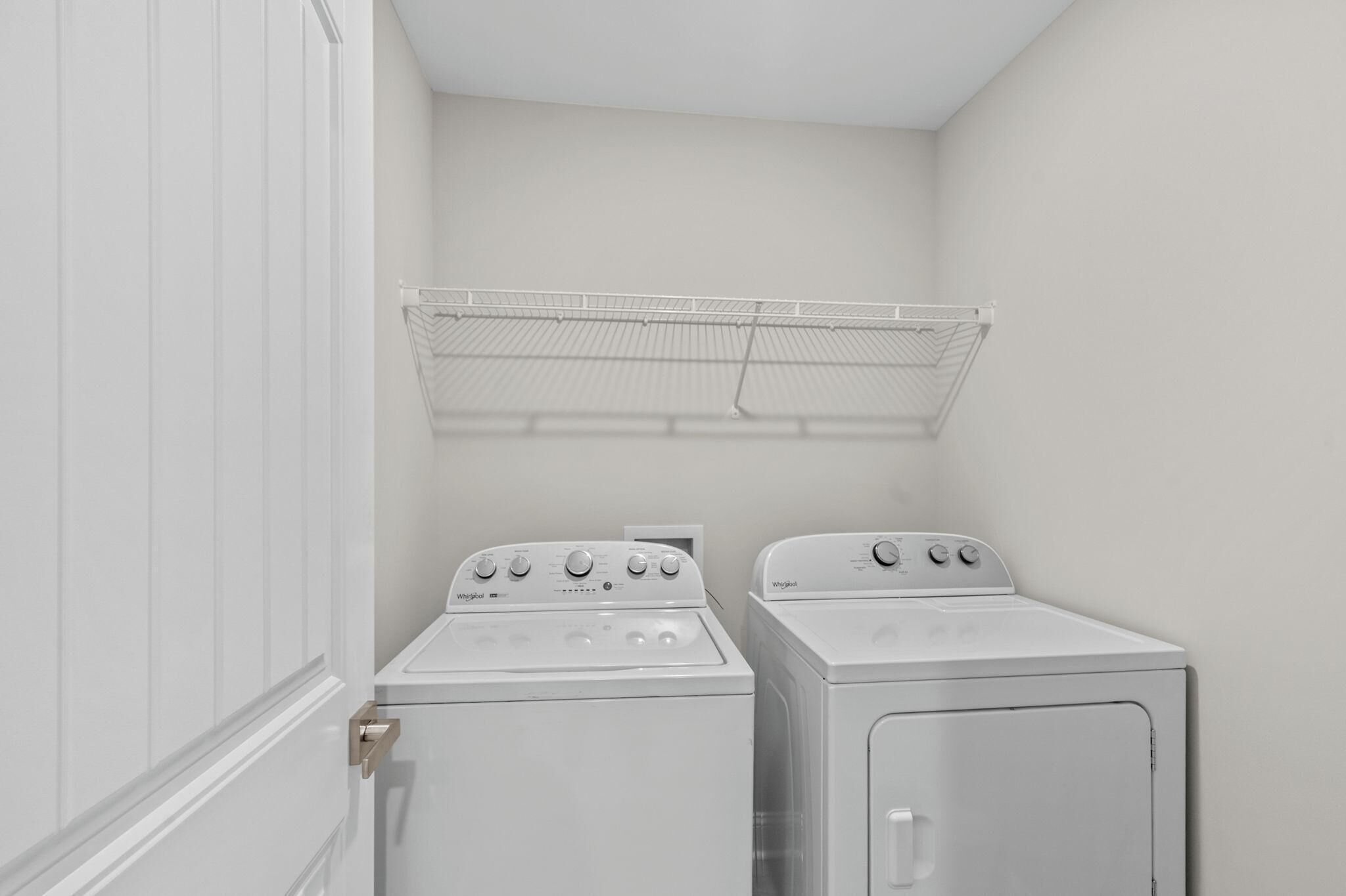 A laundry room with two white Whirlpool washers and dryers, a metal drying rack, and a white door.