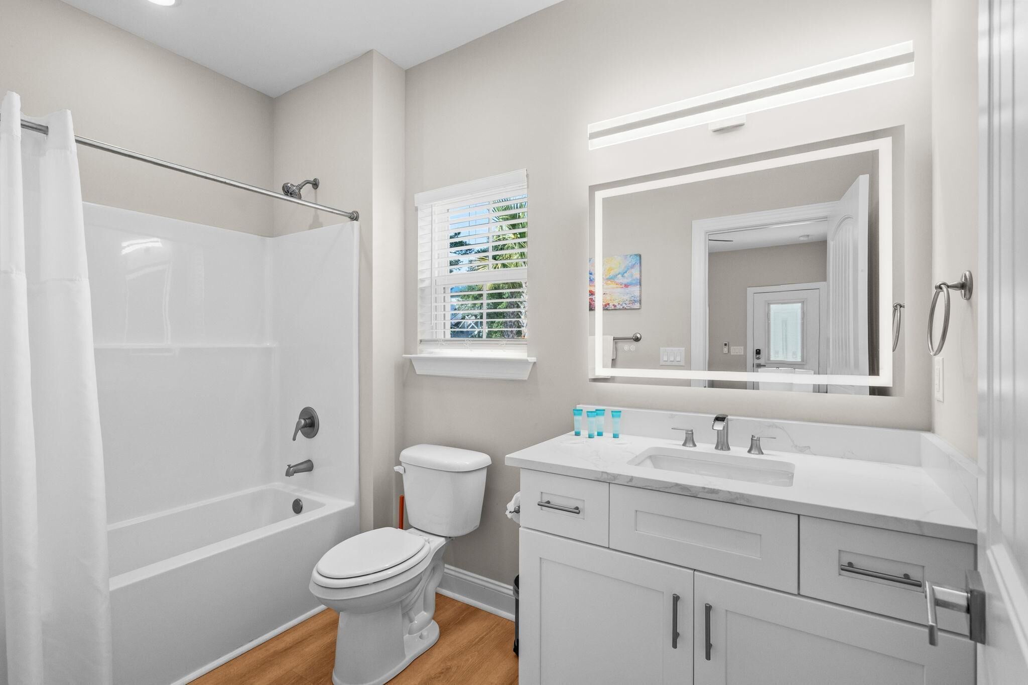 A modern bathroom with a bathtub, toilet, vanity, and a large mirror.