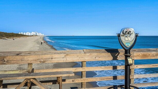 A wooden pier with a metal binoculars stand, overlooking a beach with buildings in the distance. - The Pink Panther-ocean Side-pet Friendly (Myrtle Beach)
