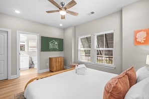 Quarto com cama, ventilador de teto, placa verde e janela com persianas.