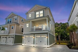 Un immeuble résidentiel à plusieurs étages doté d’un balcon, de deux portes de garage et d’une pelouse bien entretenue.