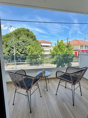A balcony with two wicker chairs and a small table, overlooking a residential area with trees and buildings. - Το BO Suites είναι ένα ολοκαίνουργιο συγκρότημα διαμερισμάτων στα Ιωάννινα. (Kato Neochoropoulo)