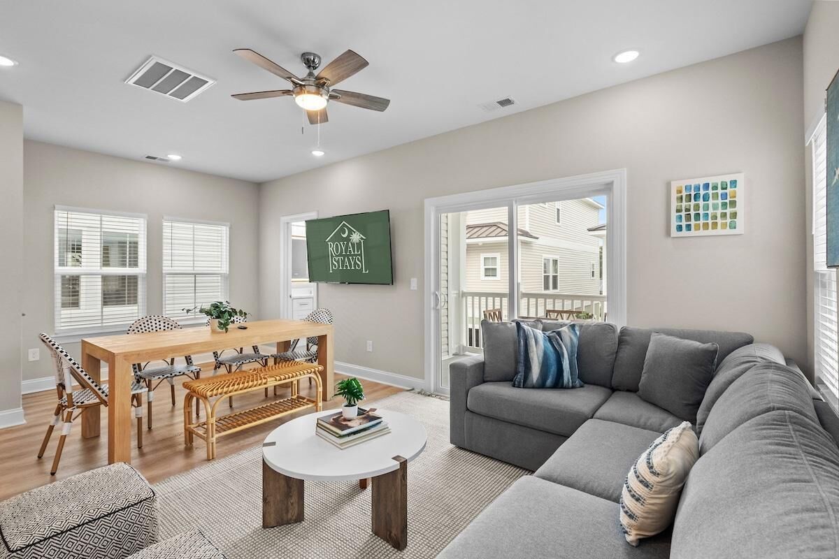 A modern living room with a dining area, grey sofa, and a ceiling fan.
