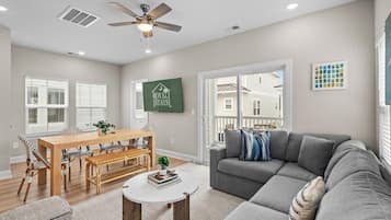 A modern living room with a dining area, grey sofa, and a ceiling fan.