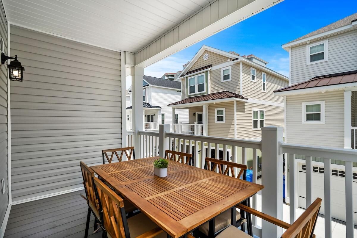 Ein überdachter Balkon mit Holztisch und -stühlen, einem Blumentopf und einem weißen Geländer.