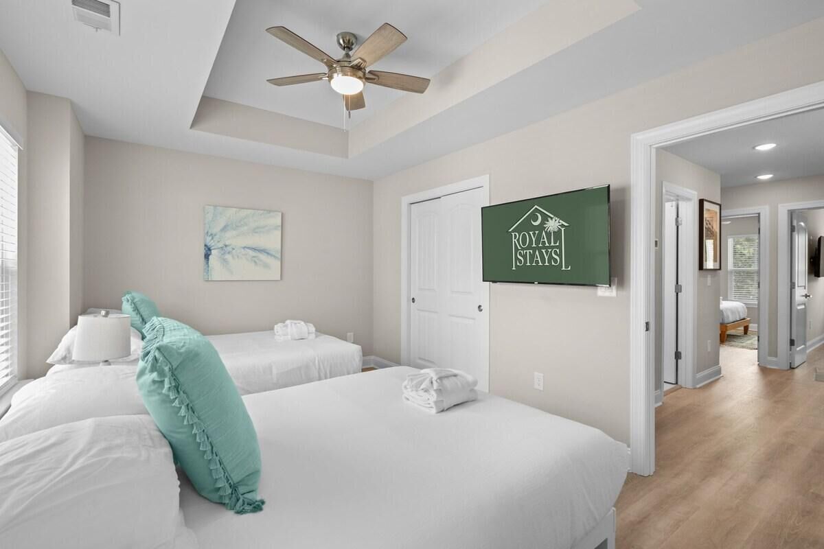 A hotel room with two beds, a ceiling fan, a painting, and a sign that reads "ROYAL STAYS".
