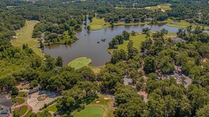 Vista aérea de un campo de golf con varios estanques, rodeado de un bosque denso y un área de estacionamiento.