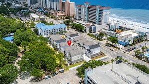 Vista aérea de una ciudad costera con una mezcla de edificios residenciales y comerciales, un hotel frente a la playa y una vista despejada del océano.