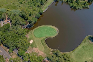 Vista aérea de un campo de golf con un estanque, rodeado de abundante vegetación y una carretera.