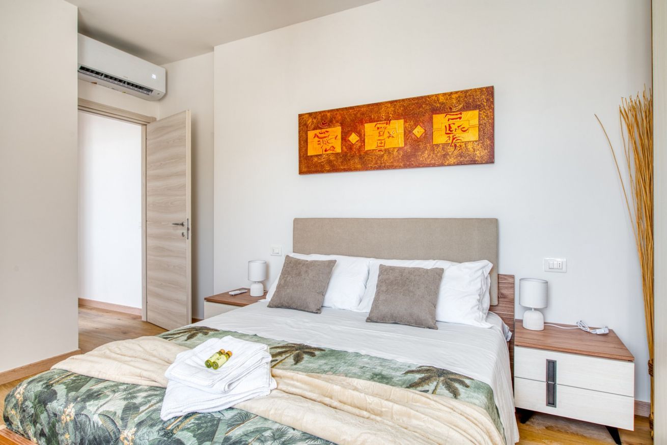 Een hotelkamer met een bed, nachtkastje, een schilderij aan de muur en een deur.