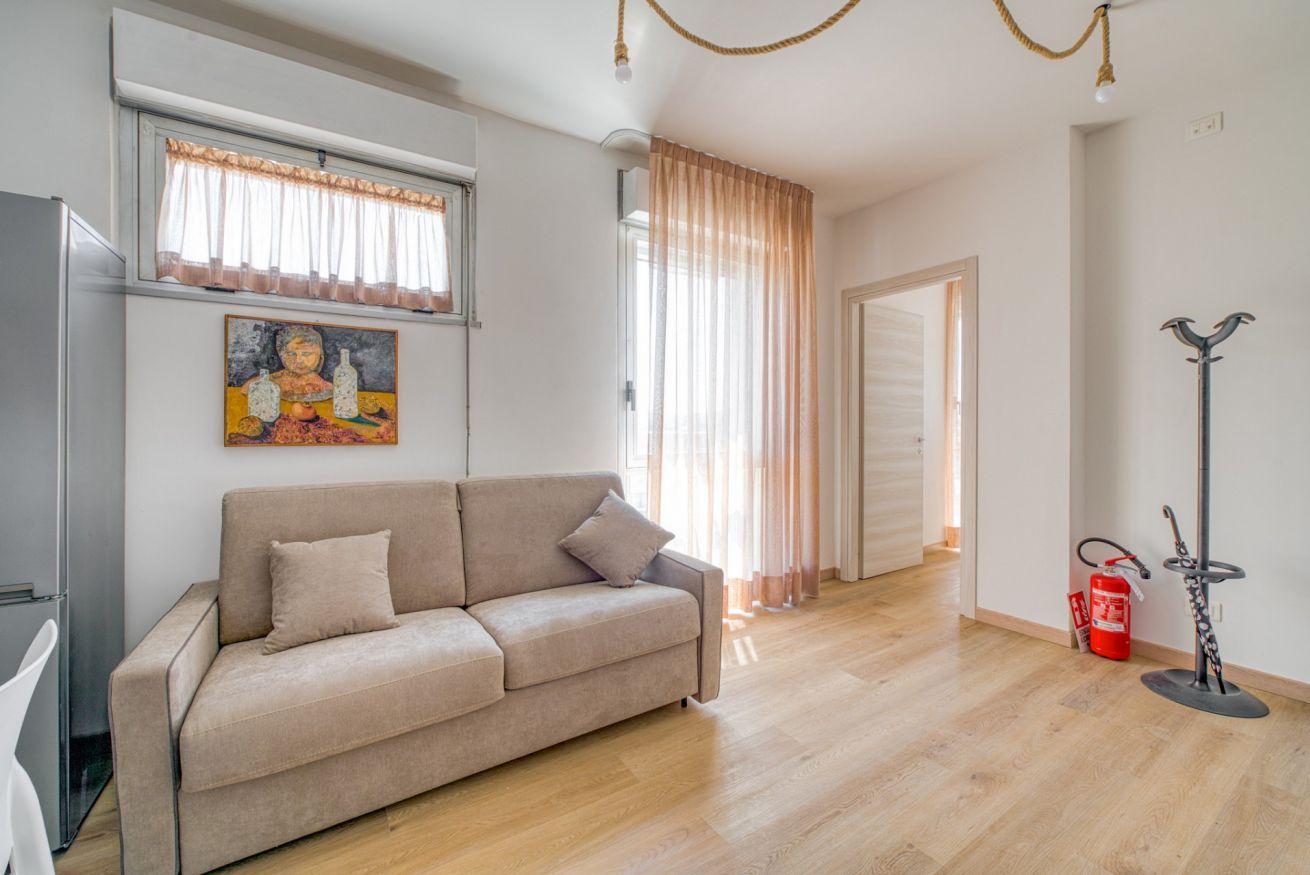A living room with a sofa, a painting, a window with curtains, and a fire extinguisher.