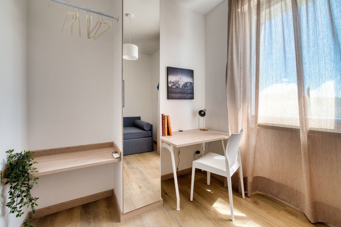 A room with a desk, chair, hanging clothes rack, and a plant.
