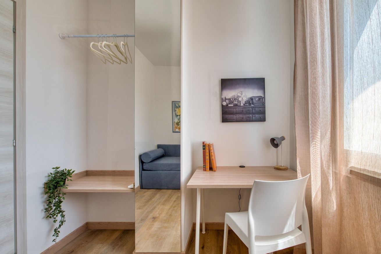 A modern room with a wooden desk, a white chair, a grey sofa, and a wall-mounted picture.