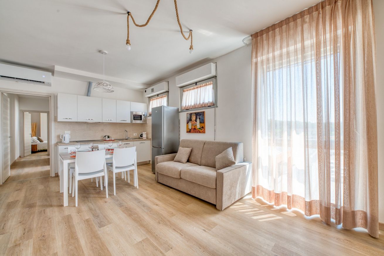 Ein modernes Wohnzimmer mit einer Couch, einem Esstisch und Stühlen. Es gibt eine Küchenzeile mit Schränken und Geräten.