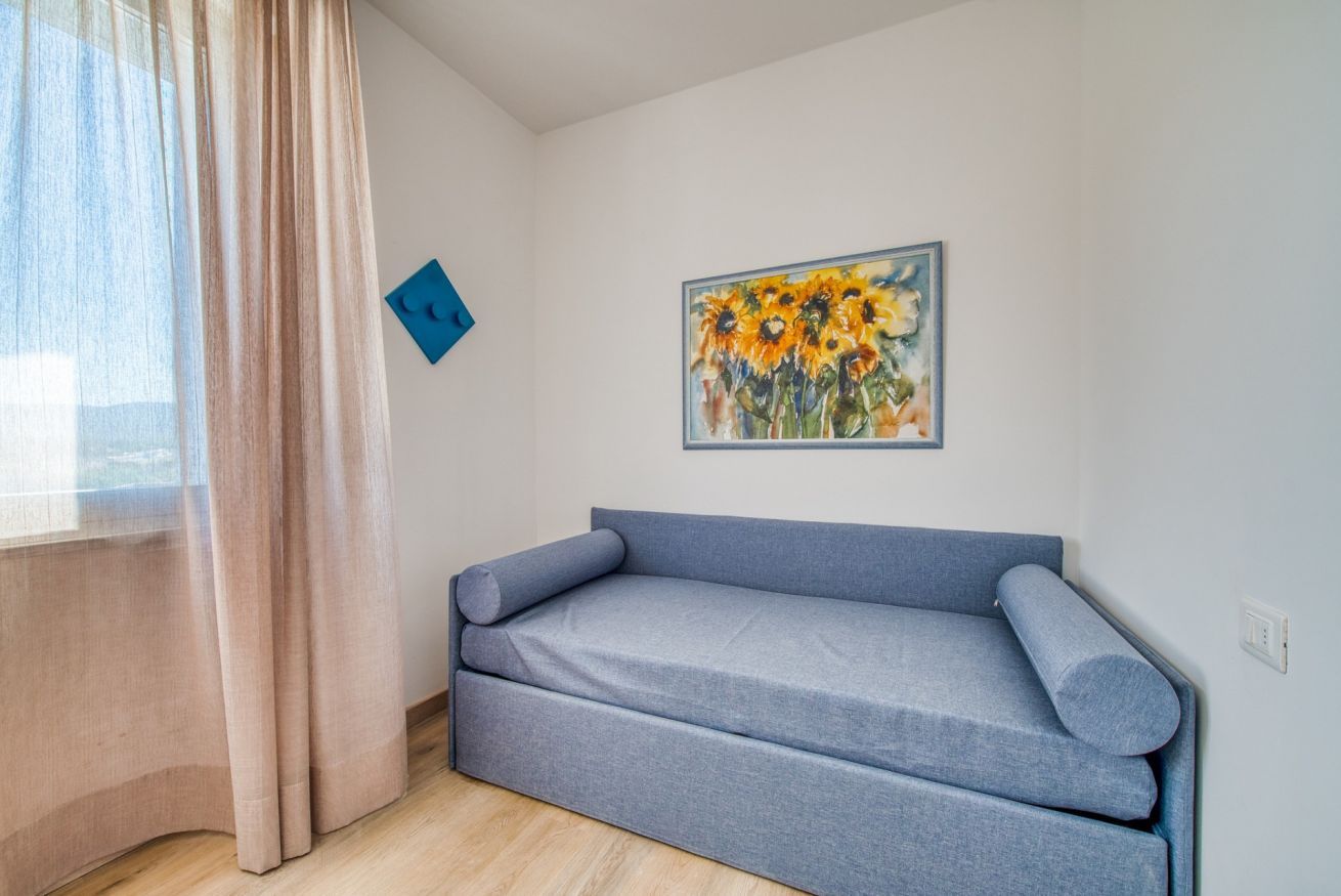 Ein Zimmer mit einer Couch, einem Sonnenblumenbild, einer blauen Akzentwand und einem Fenster mit Vorhängen.