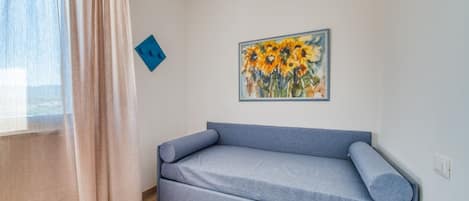 A room with a sofa, a painting of sunflowers, a blue accent wall, and a window with curtains.