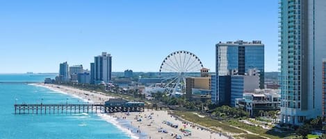 A coastal cityscape with a beach, a pier, and a large Ferris wheel.