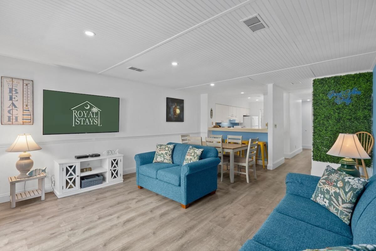 Una sala de estar moderna con un sofá azul, un comedor y una cocina al fondo.