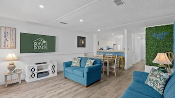 A modern living room with a blue sofa, a dining area, and a kitchen in the background.
