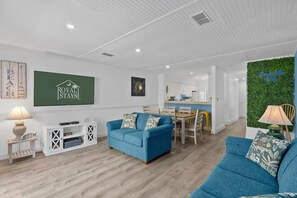 A modern living room with a blue sofa, a dining area, and a kitchen in the background. - Myrtle Dunes- Across From Beach, Pet Friendly (Myrtle Beach)