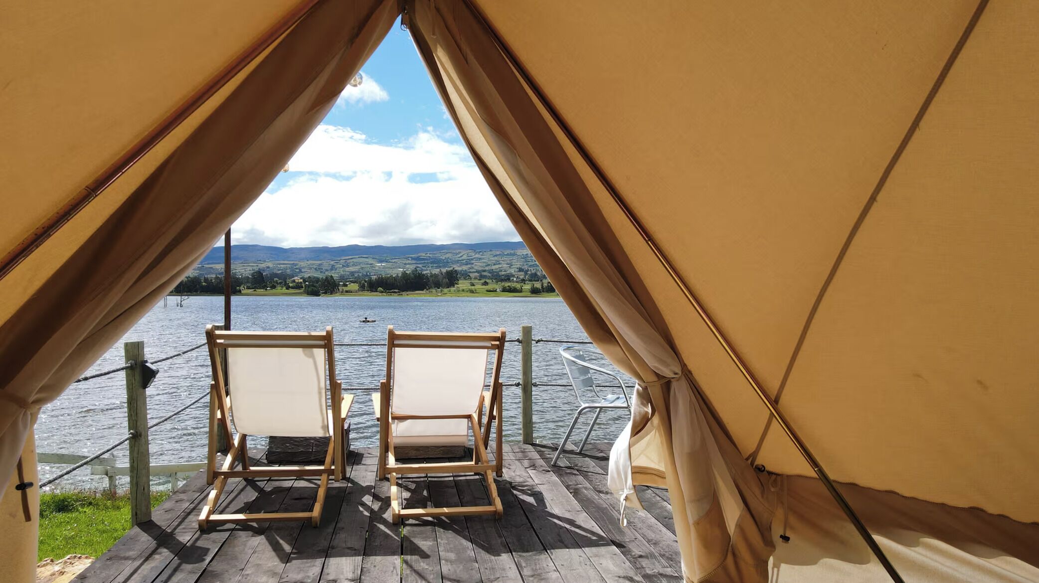 A tent with two wooden chairs facing a lake.