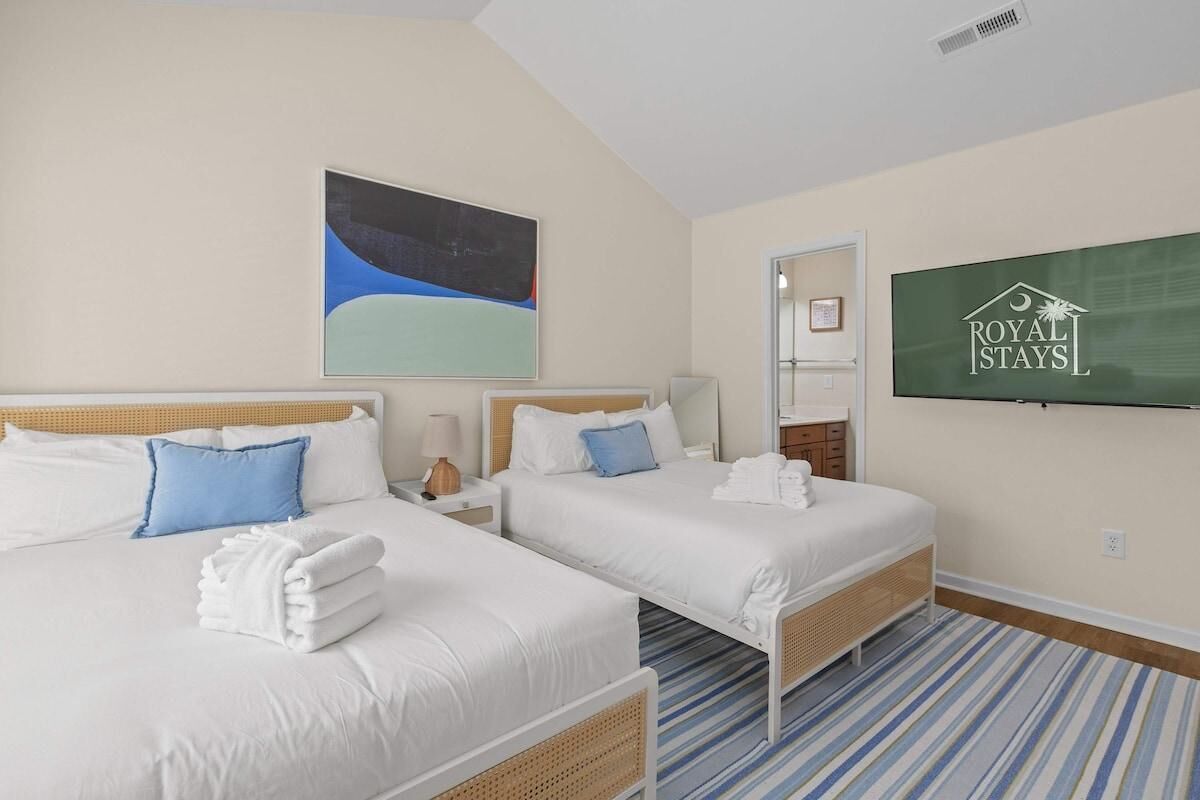 A hotel room with two beds, a large painting, a television, and a striped carpet.