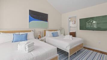 A hotel room with two beds, a large painting, a television, and a striped carpet.