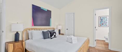 A bedroom with a wooden bed, white bedding, a ceiling fan, and a large abstract painting on the wall.