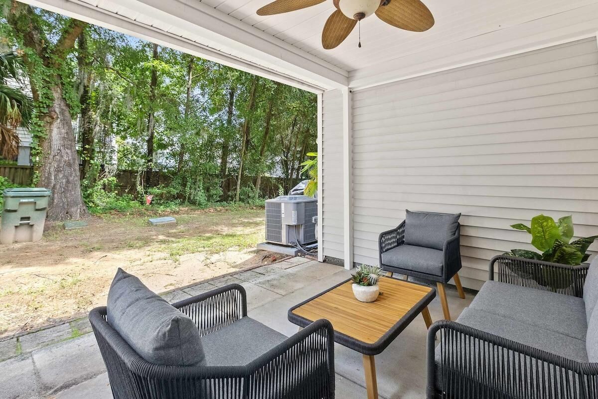 A covered patio with wicker furniture, a ceiling fan, and a view of a backyard with trees and a grill.