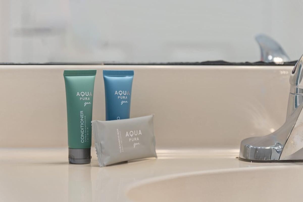 A bathroom sink with two bottles of AQUA PURA conditioner and a small packet of the product.