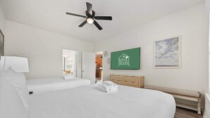 A hotel room with two beds, a ceiling fan, a green sign with 'ROYAL STAYS' logo, a framed picture on the wall, and a bench. - Myrtle Golf Escape At Legends-pool-pet Friendly (Myrtle Beach)