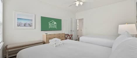 A hotel room with a large bed, a ceiling fan, a framed picture on the wall, and a sign for 'ROYAL STAYS'.