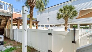Un giardino recintato con un patio in legno, palme e una staccionata bianca.