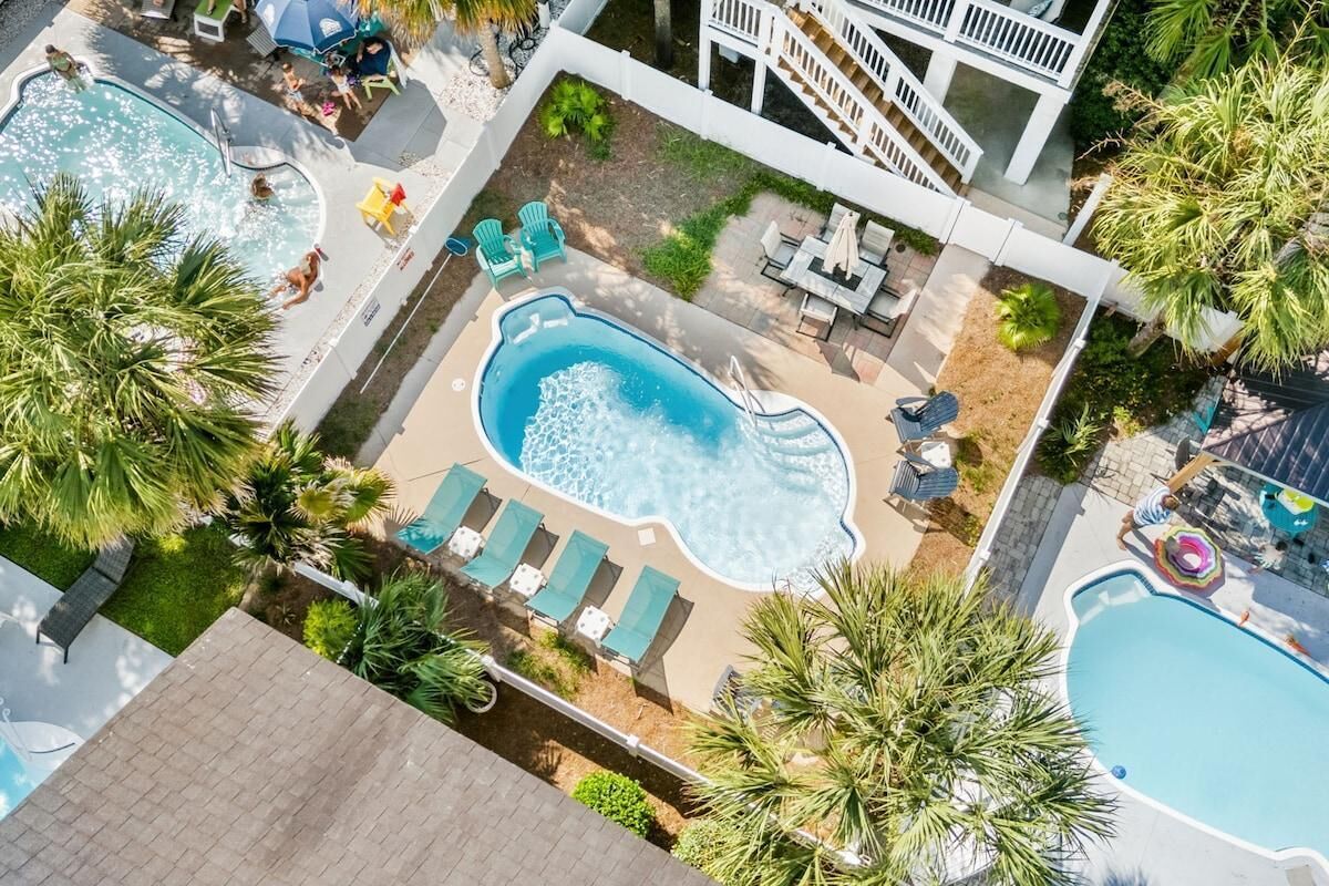 A rooftop pool area with multiple pools, lounge chairs, and a staircase leading to an upper level.